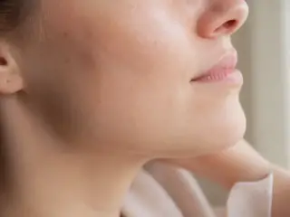 Joue et pommette d’une femme, photographiées de profil rapproché, lumière douce de fenêtre, peau claire, personne non identifiable