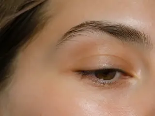 Œil et sourcil d’une femme en gros plan, paupière légèrement abaissée, lumière douce de fenêtre, personne non identifiable