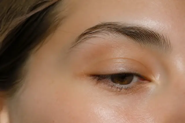 Œil et sourcil d’une femme en gros plan, paupière légèrement abaissée, lumière douce de fenêtre, personne non identifiable