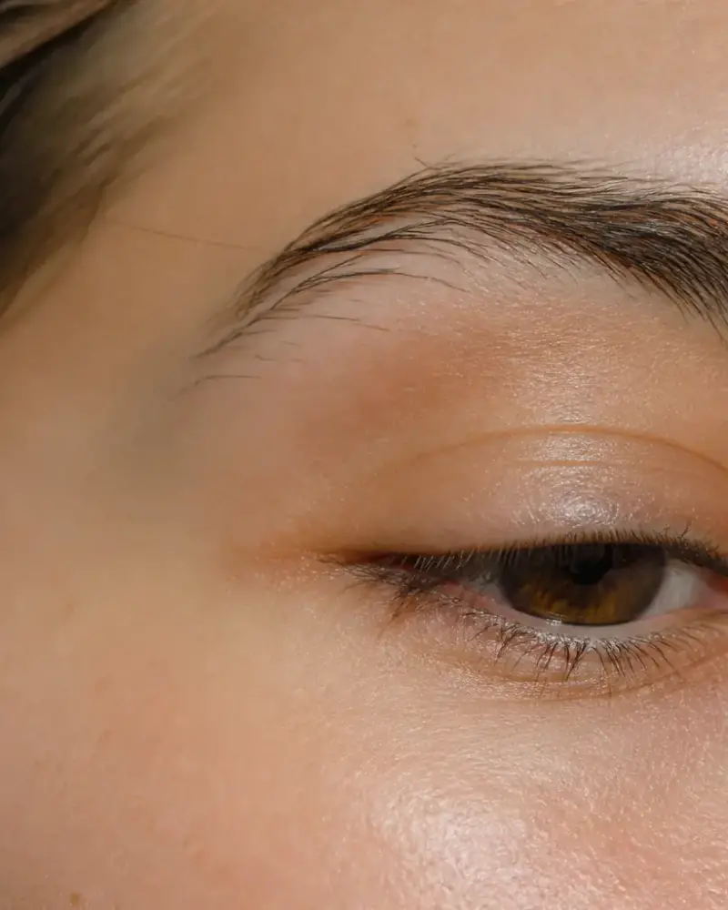 Œil et sourcil d’une femme en gros plan, paupière légèrement abaissée, lumière douce de fenêtre, personne non identifiable