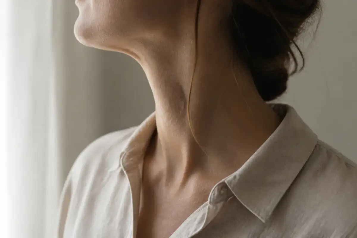 Profil d’un cou et d’une mâchoire de femme, cadré de sous la bouche jusqu’au col d’un chemisier de lin, lumière douce de fenêtre