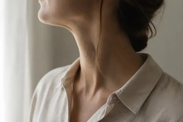 Profil d’un cou et d’une mâchoire de femme, cadré de sous la bouche jusqu’au col d’un chemisier de lin, lumière douce de fenêtre