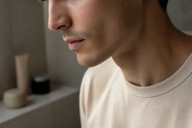 Profil d’un visage d’homme penché légèrement vers le bas, éclairage doux de fenêtre, ligne de la mâchoire visible, personne non identifiable